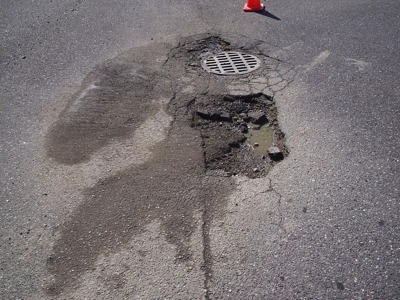 A broken pothole around a storm drain before repair